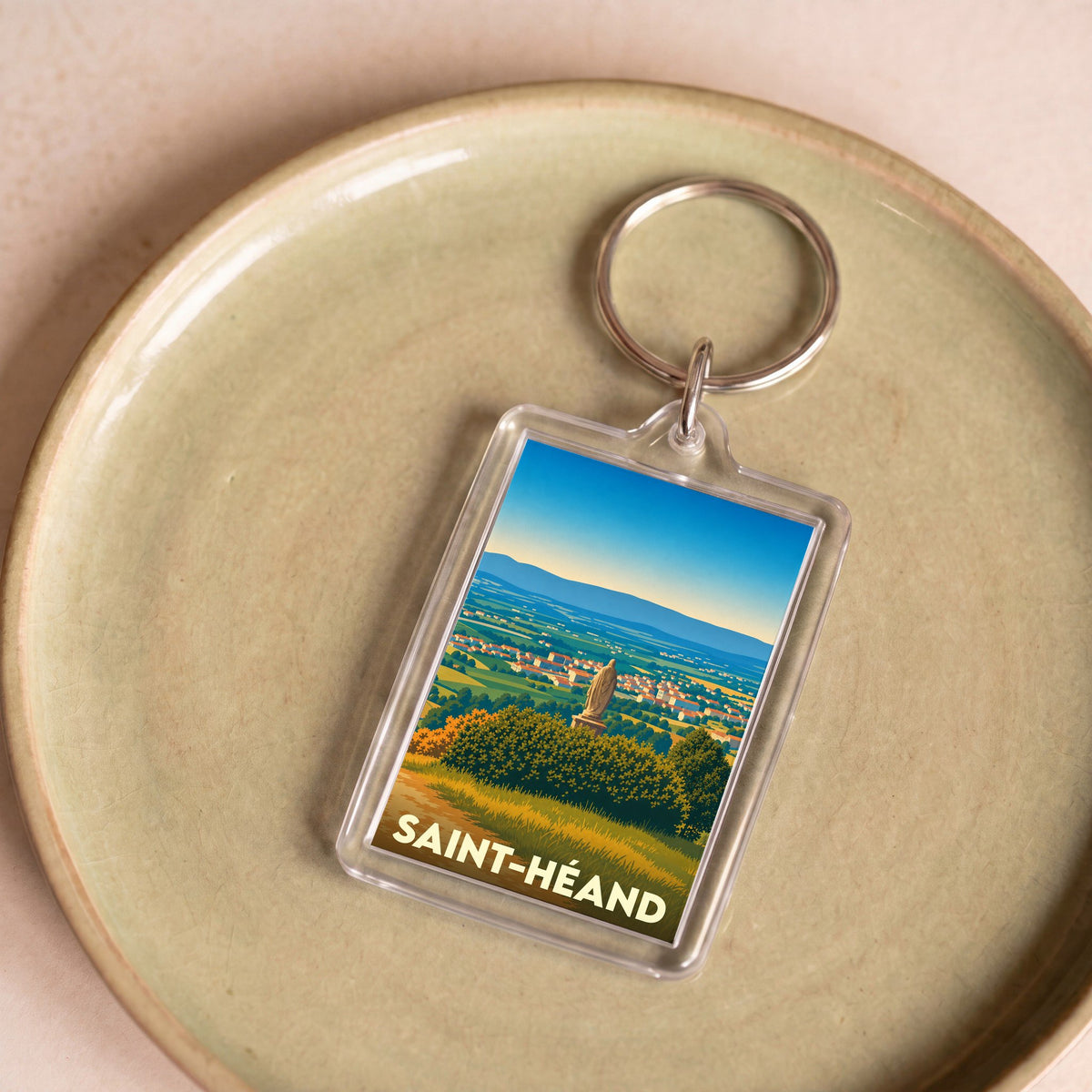 Porte-clés souvenir de la ville de Saint-Héand avec une illustration stylisée de son paysage.