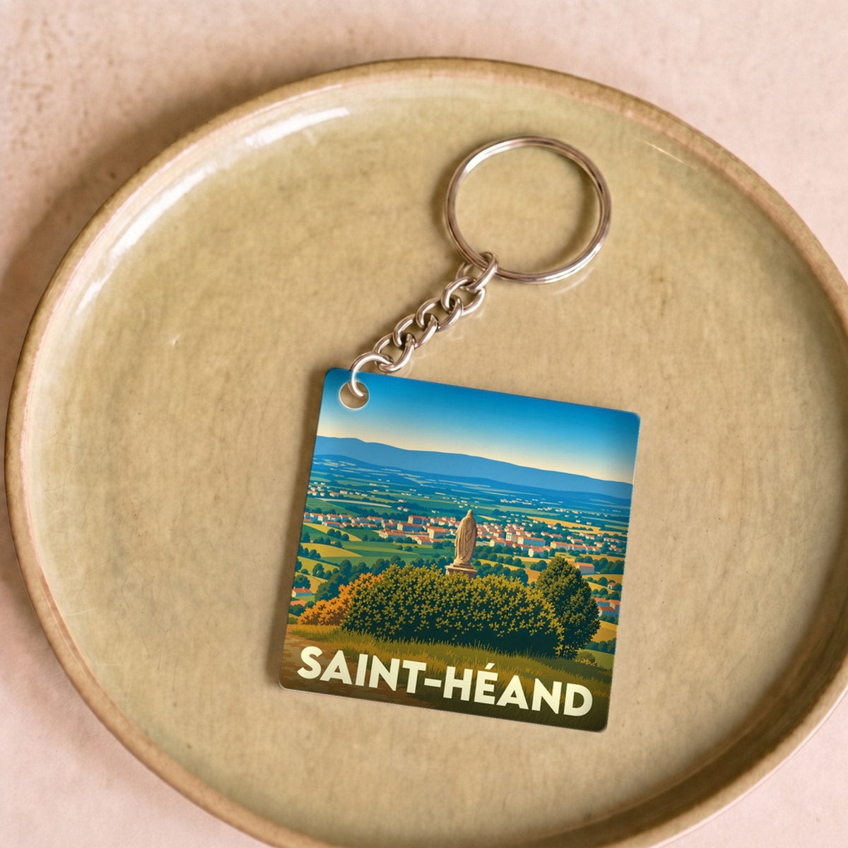 Porte-clés souvenir de la ville de Saint-Héand avec une illustration stylisée d'un paysage panoramique.