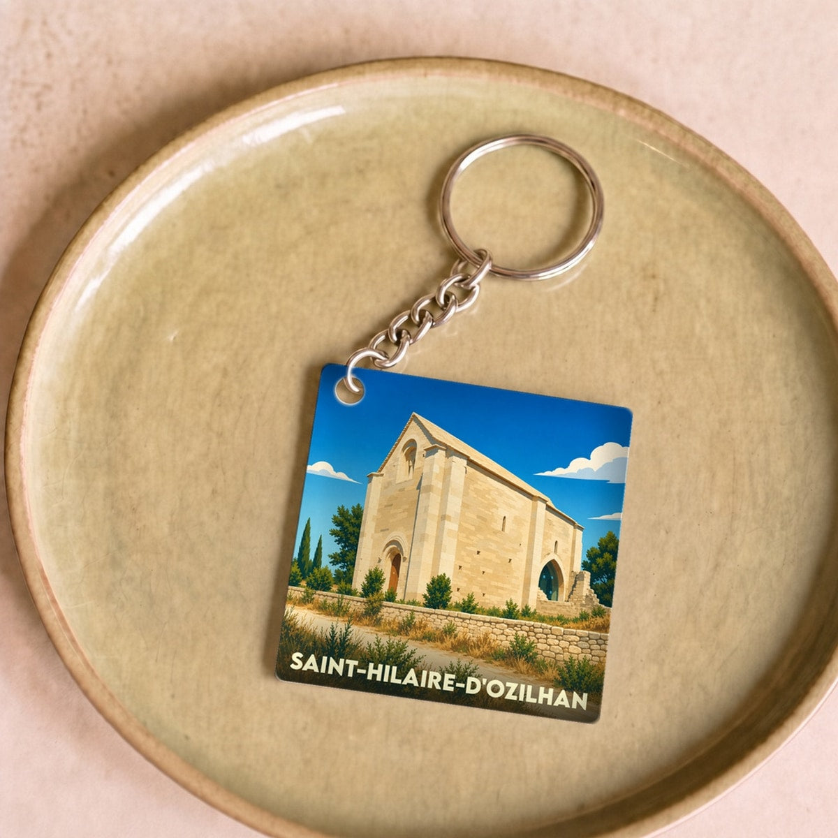 Porte-clés souvenir de la ville de Saint-Hilaire-d'Ozilhan avec une illustration stylisée de sa chapelle romane.