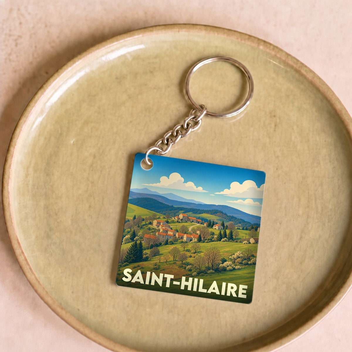 Porte-clés souvenir de la ville de Saint-Hilaire avec une illustration stylisée de paysages vallonnés.