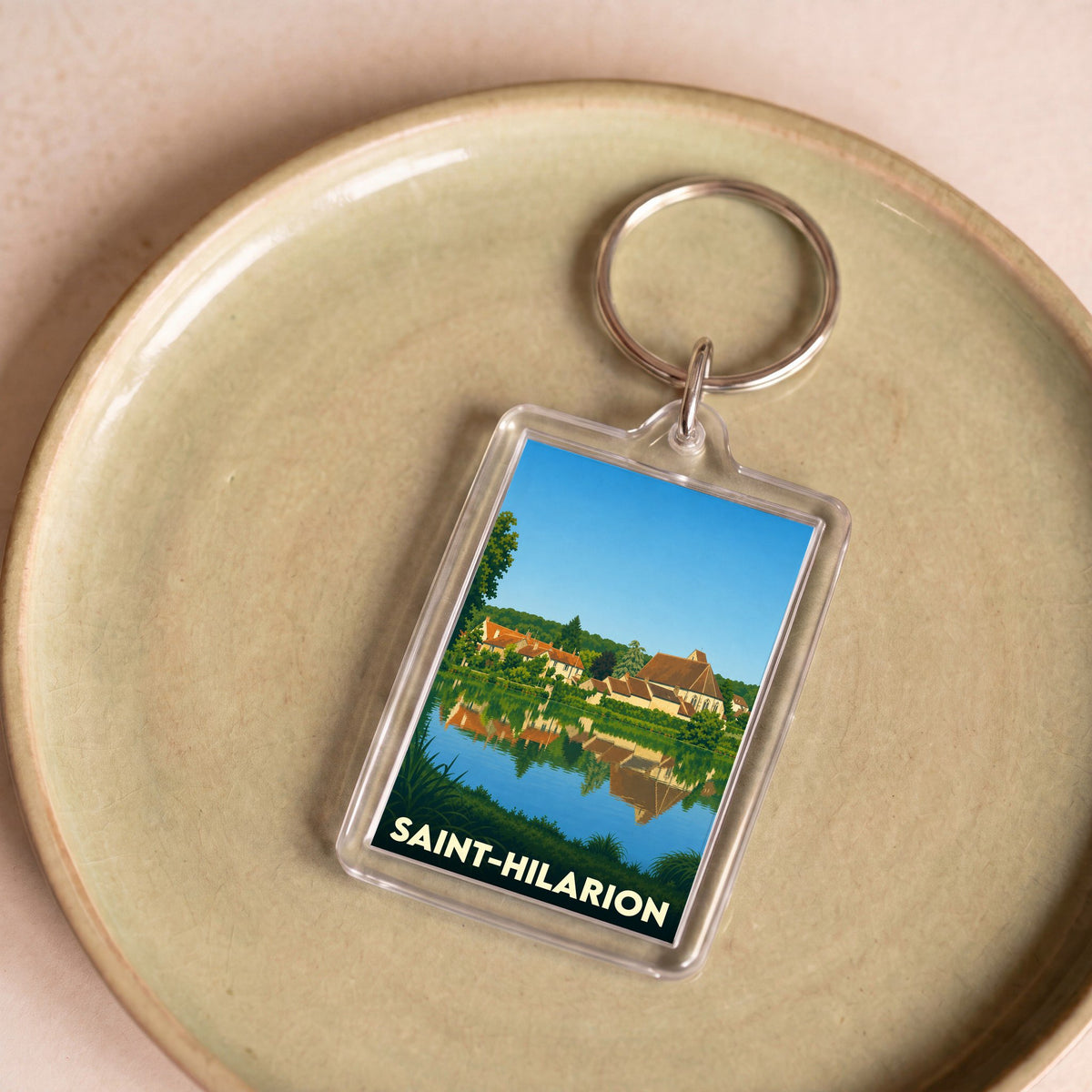 Porte-clés souvenir de la ville de Saint-Hilarion avec une illustration stylisée d'un paysage au bord de l'eau.