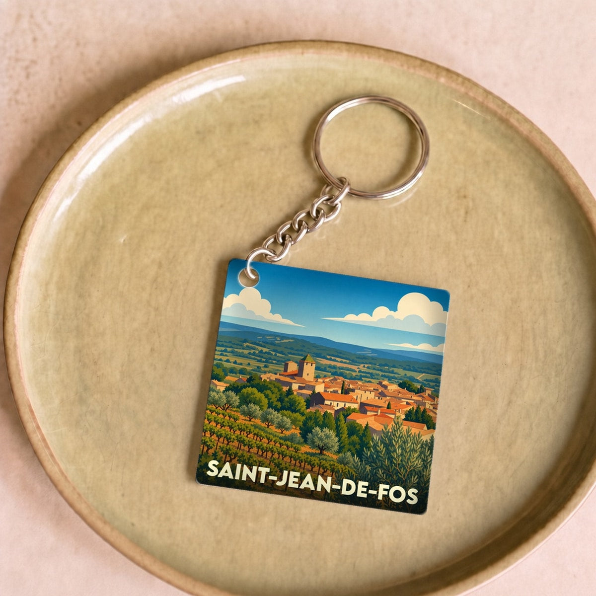 Porte-clés souvenir de la ville de Saint-Jean-de-Fos avec une illustration stylisée de son paysage et de ses vignobles.