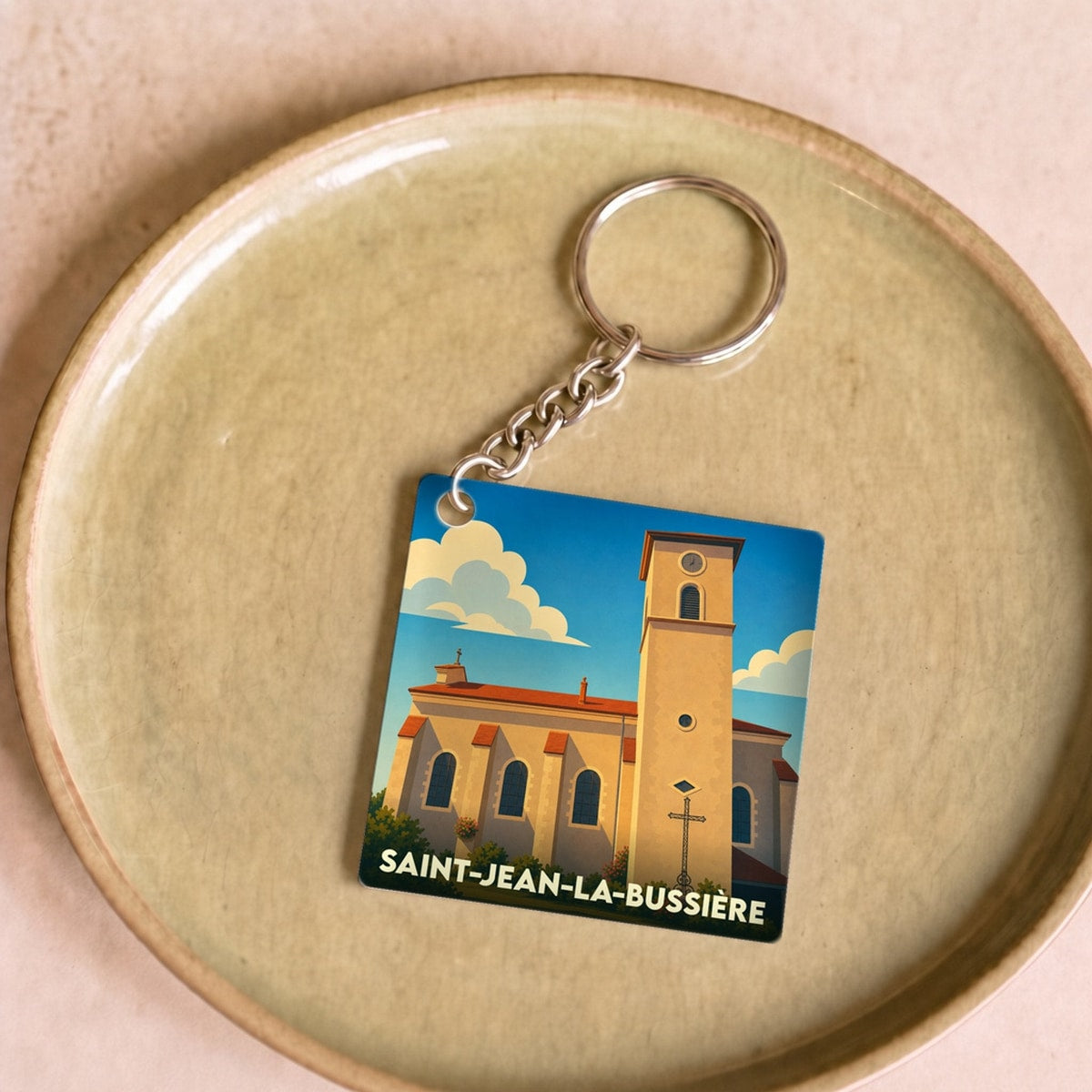 Porte-clés souvenir de la ville de Saint-Jean-la-Bussière avec une illustration stylisée de son église.