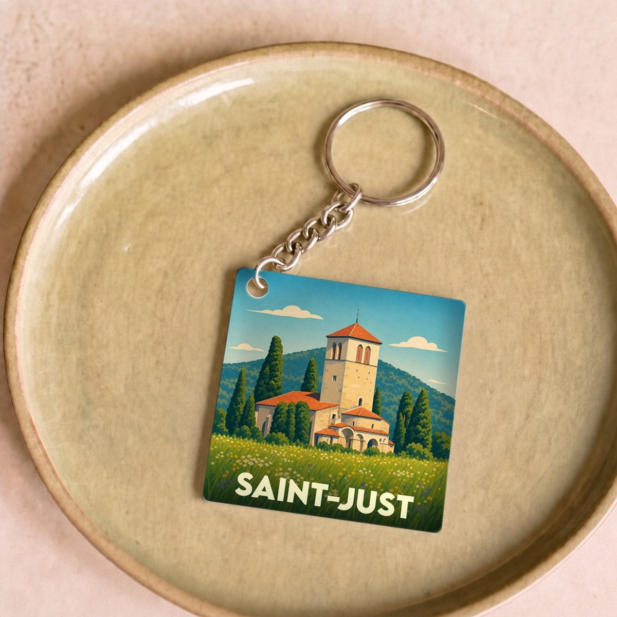 Porte-clés souvenir de la ville de Saint-Just avec une illustration stylisée d'une église et d'un paysage ensoleillé.