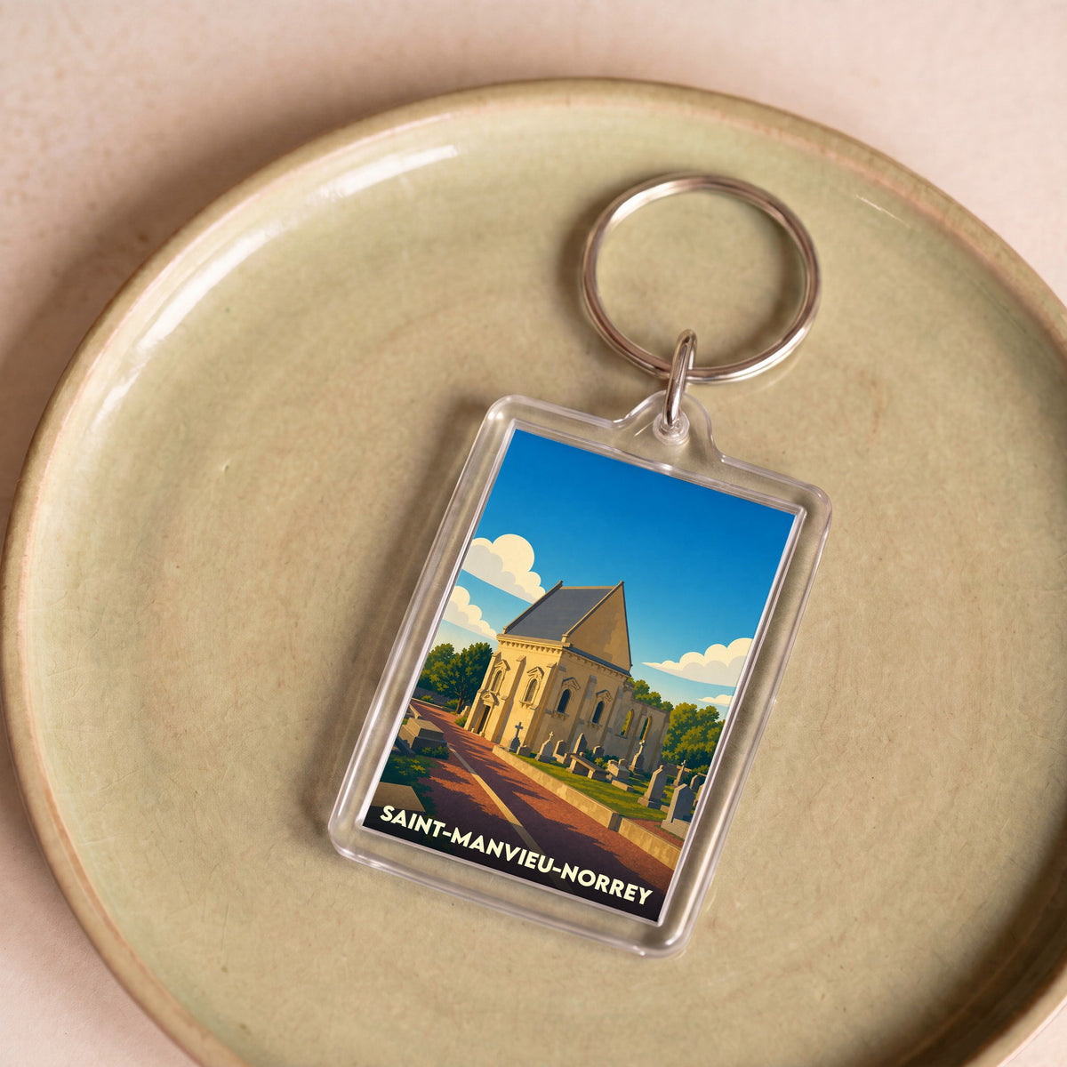 Porte-clés souvenir de la ville de Saint-Manvieu-Norrey avec une illustration stylisée de son église et de son cimetière.