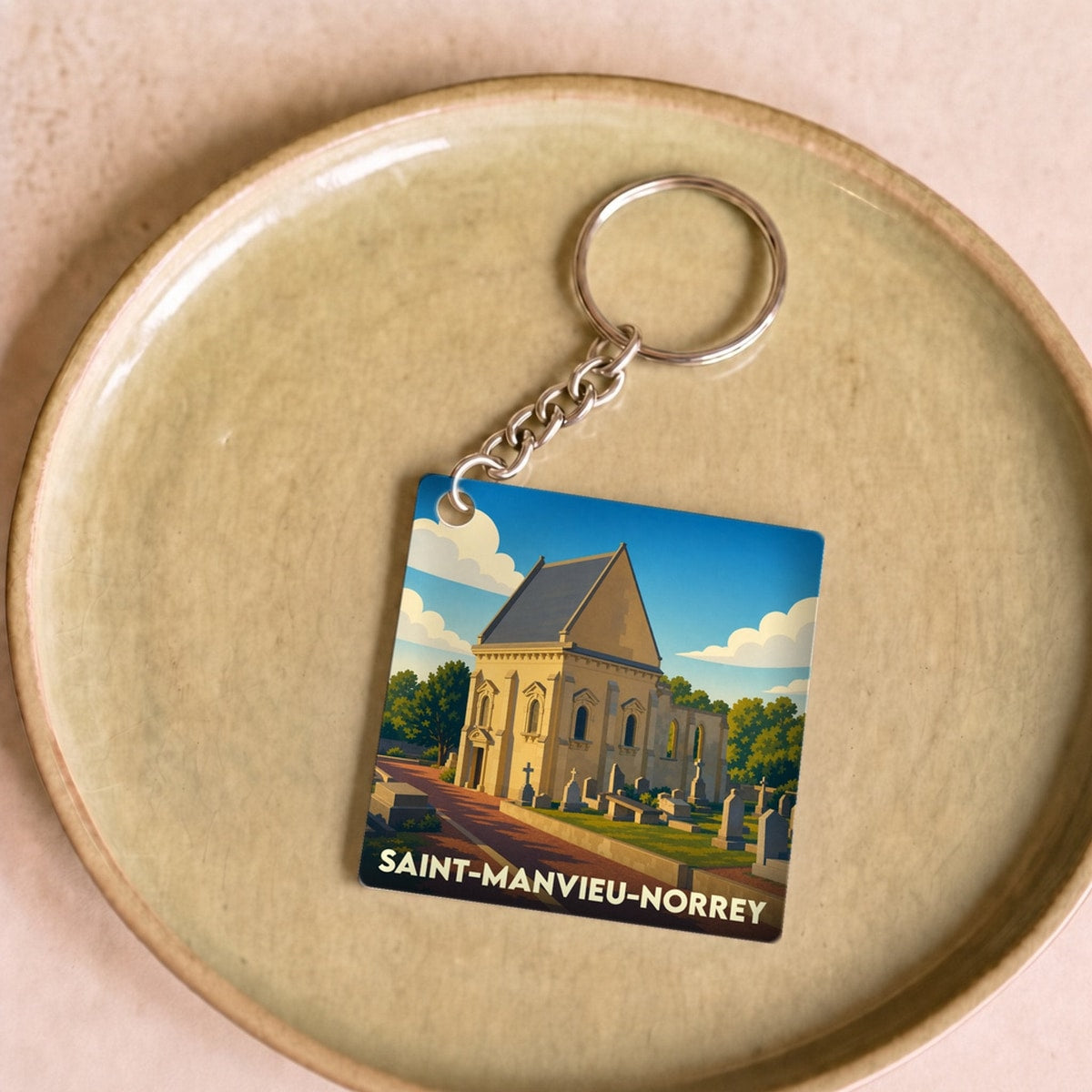 Porte-clés souvenir de la ville de Saint-Manvieu-Norrey avec une illustration stylisée de son église et de son cimetière.