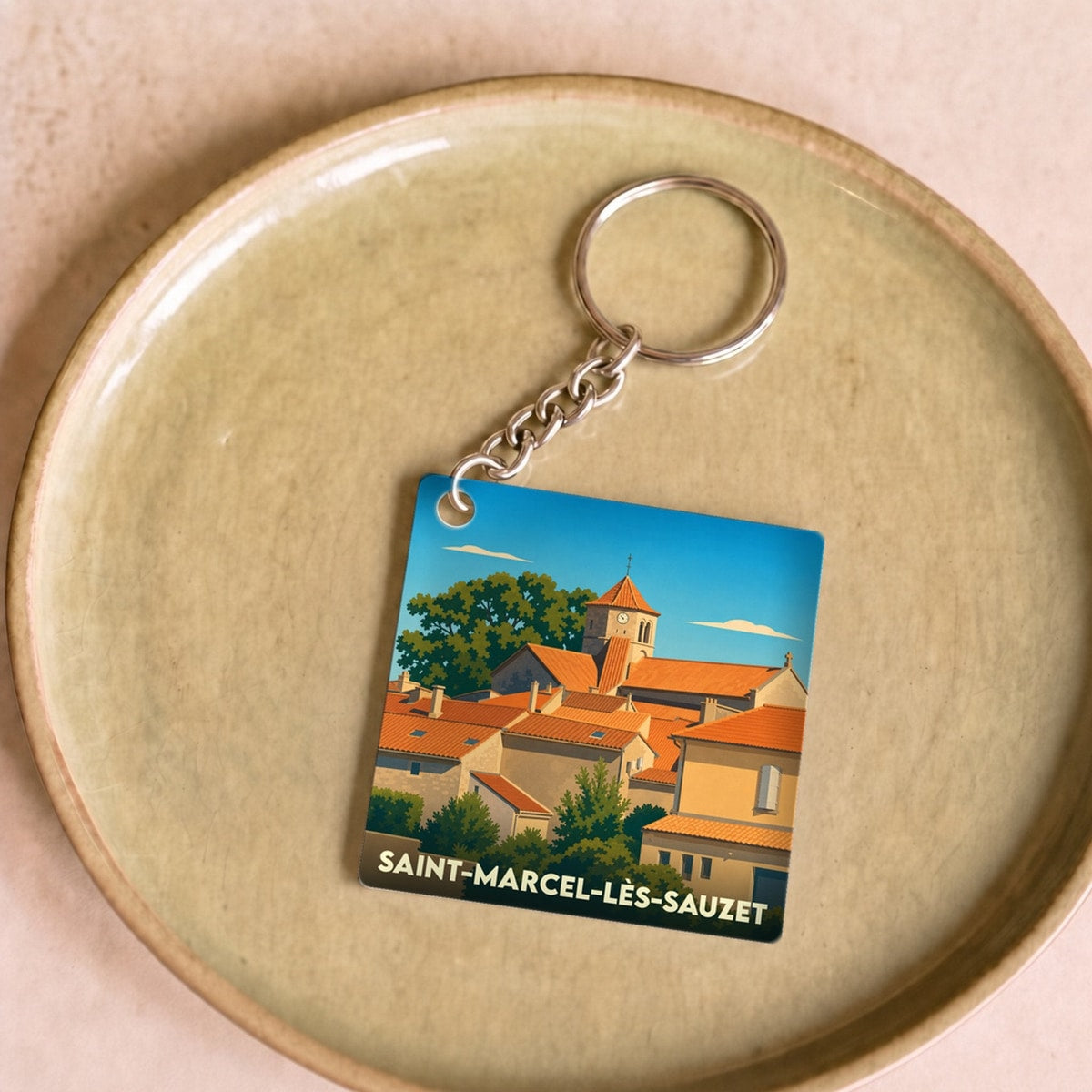 Porte-clés souvenir de Saint-Marcel-lès-Sauzet avec une illustration stylisée du village sous un ciel bleu.