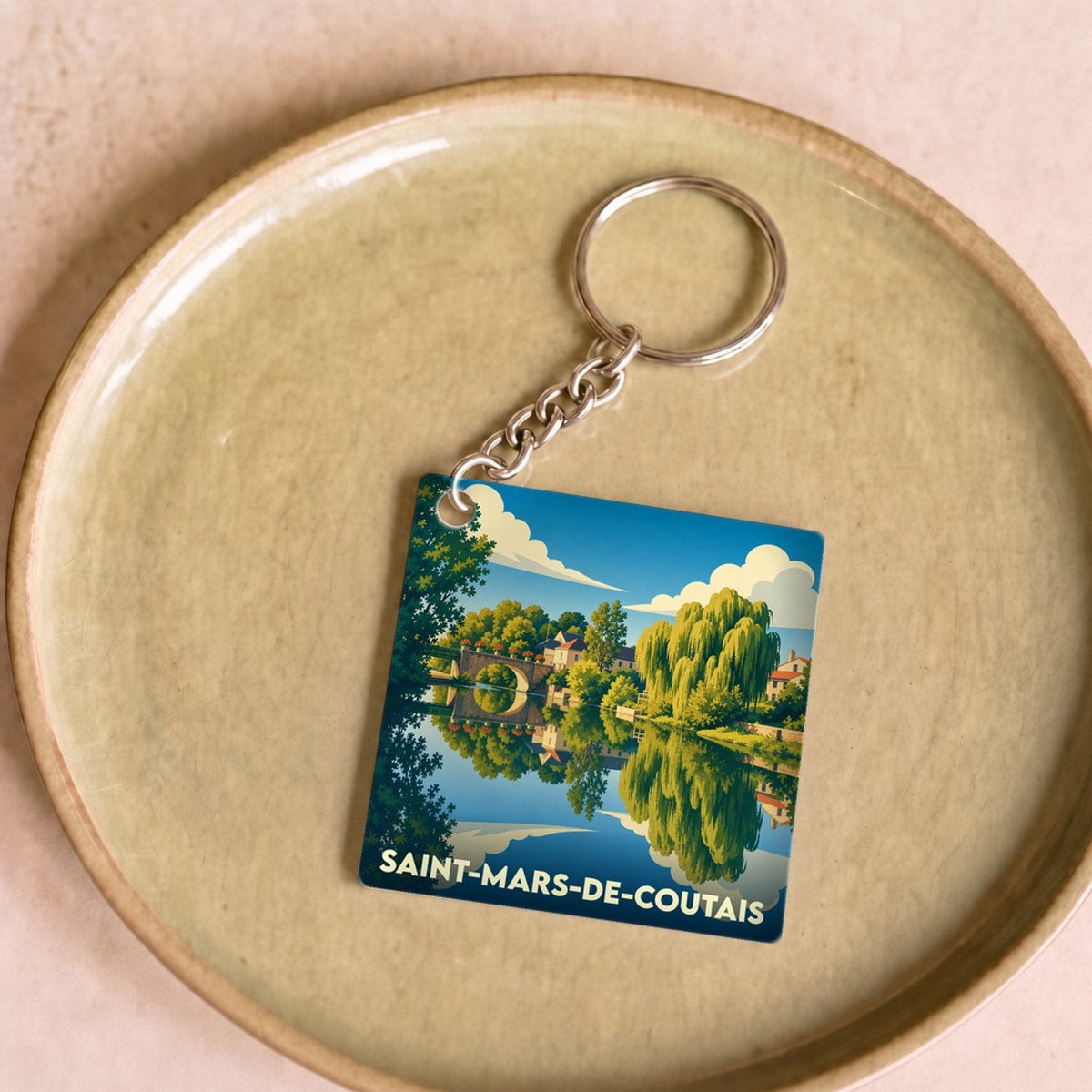 Porte-clés souvenir de Saint-Mars-de-Coutais illustré d'un paysage de rivière avec pont et saules pleureurs.
