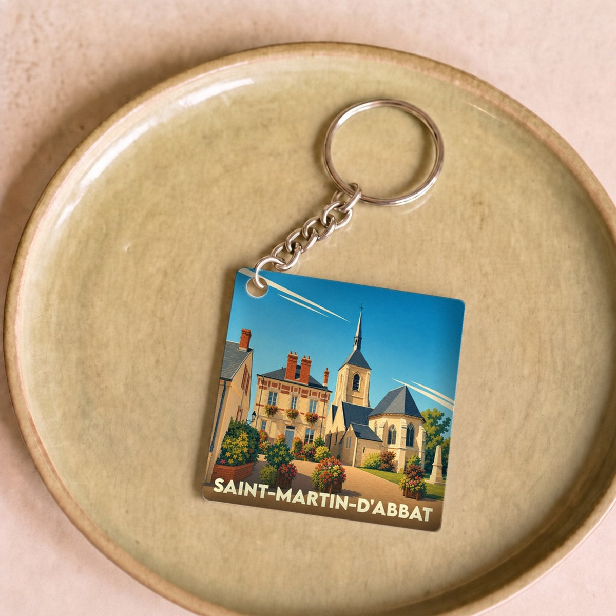 Porte-clés souvenir de la ville de Saint-Martin-d'Abbat avec une illustration stylisée d'un village fleuri.