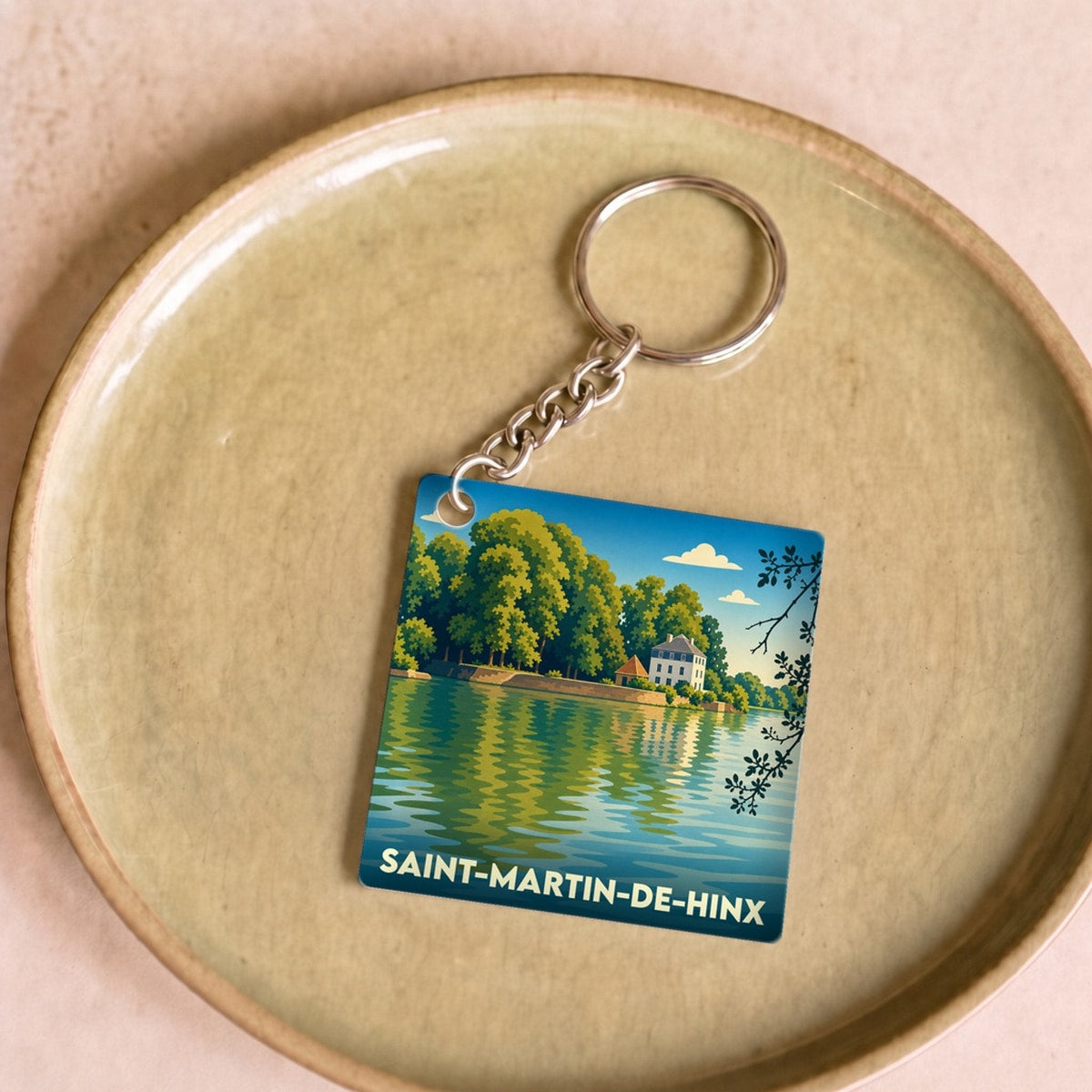 Porte-clés souvenir de la ville de Saint-Martin-de-Hinx avec une illustration stylisée d'un paysage de bord d'eau.