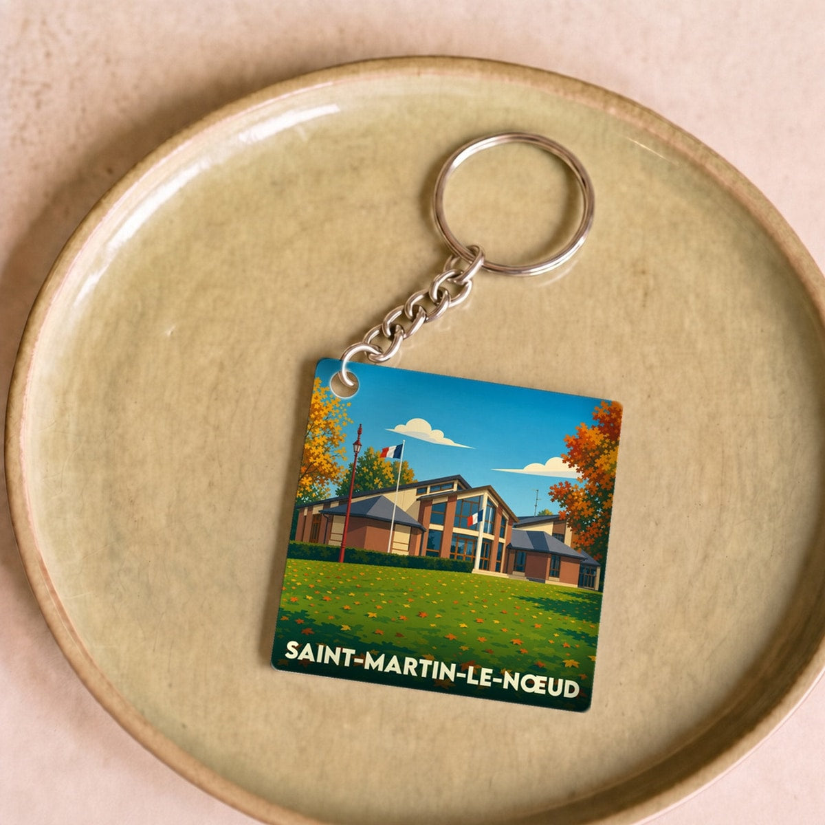 Porte-clés souvenir de la ville de Saint-Martin-le-Nœud avec une illustration stylisée d'un bâtiment sous un ciel bleu.