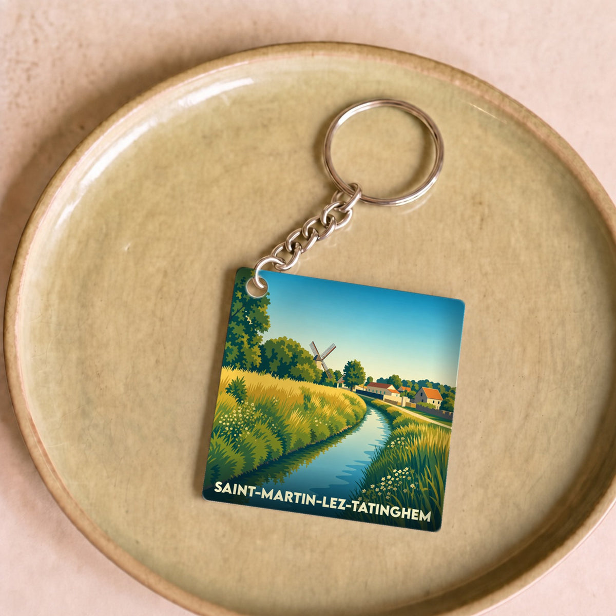 Porte-clés souvenir de la ville de Saint-Martin-lez-Tatinghem avec une illustration stylisée d'un paysage champêtre.