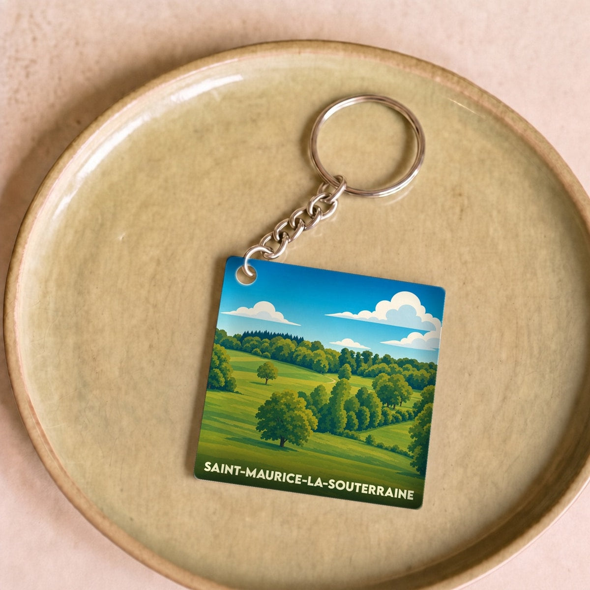 Porte-clés souvenir de la ville de Saint-Maurice-la-Souterraine avec une illustration stylisée de paysages vallonnés.