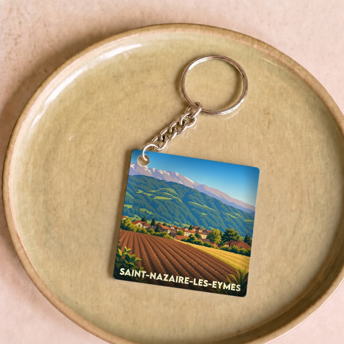 Porte-clés souvenir de la ville de Saint-Nazaire-les-Eymes avec une illustration stylisée de paysages montagneux.