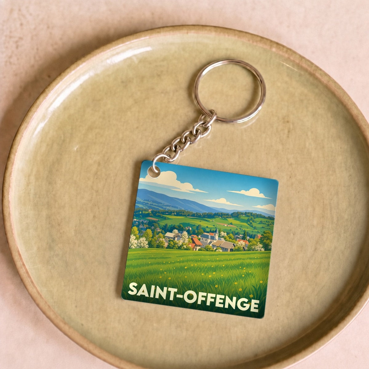 Porte-clés souvenir de la ville de Saint-Offenge avec une illustration stylisée d'un paysage champêtre.