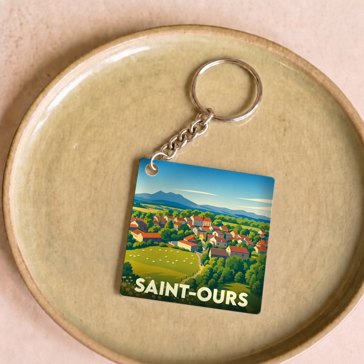Porte-clés souvenir de la ville de Saint-Ours avec une illustration stylisée de paysages vallonnés.