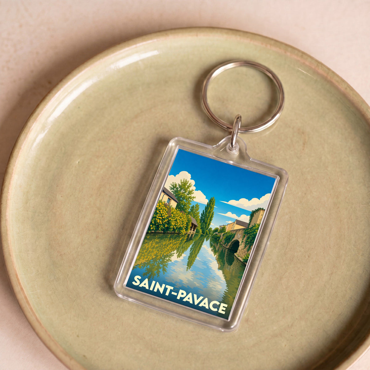 Porte-clés souvenir de la ville de Saint-Pavace avec une illustration stylisée d'un cours d'eau bordé de verdure.