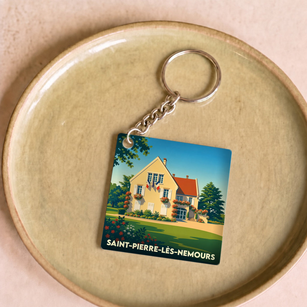 Porte-clés souvenir de la ville de Saint-Pierre-lès-Nemours avec une illustration stylisée d'une maison fleurie.