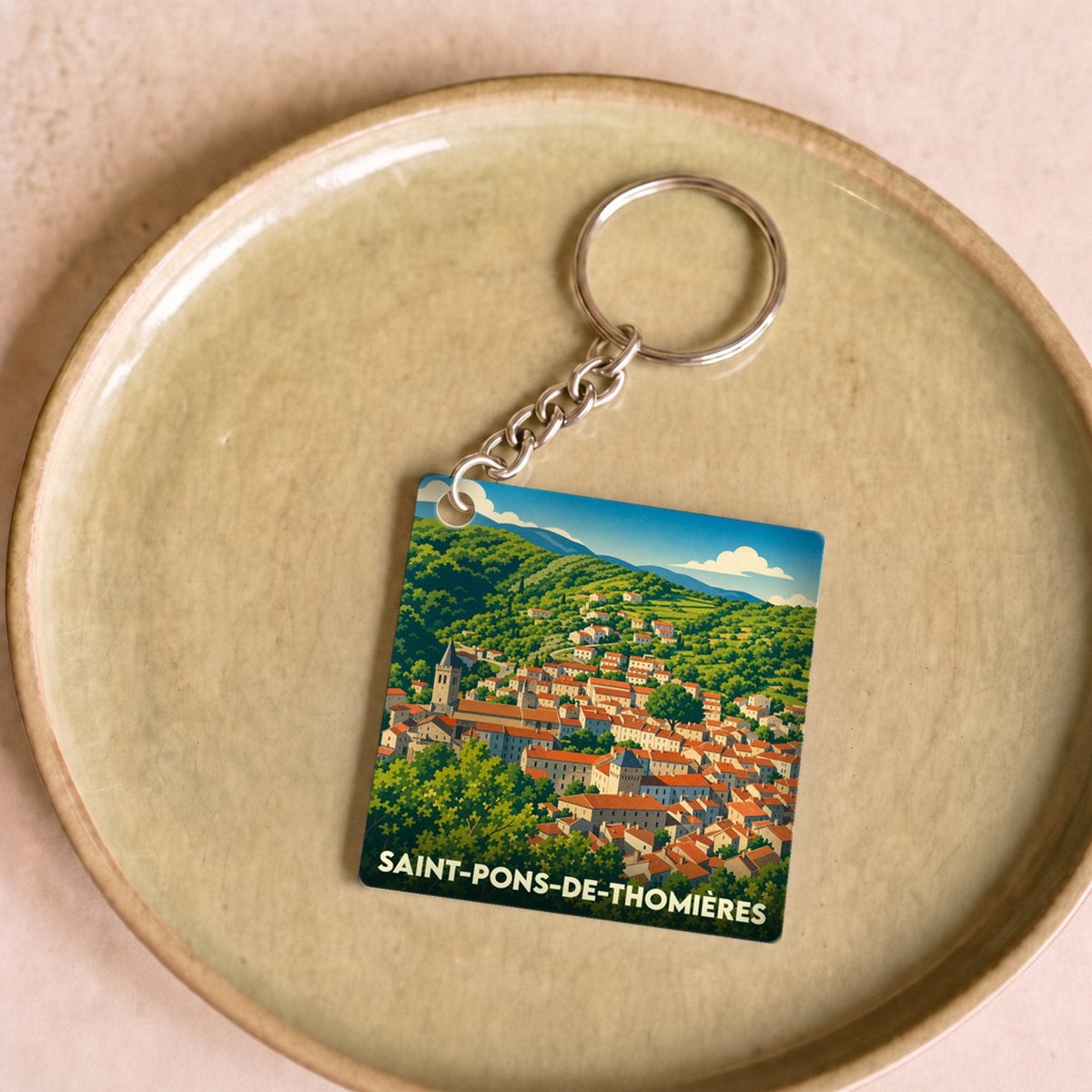 Porte-clés souvenir de la ville de Saint-Pons-de-Thomières avec une illustration paysagère stylisée.