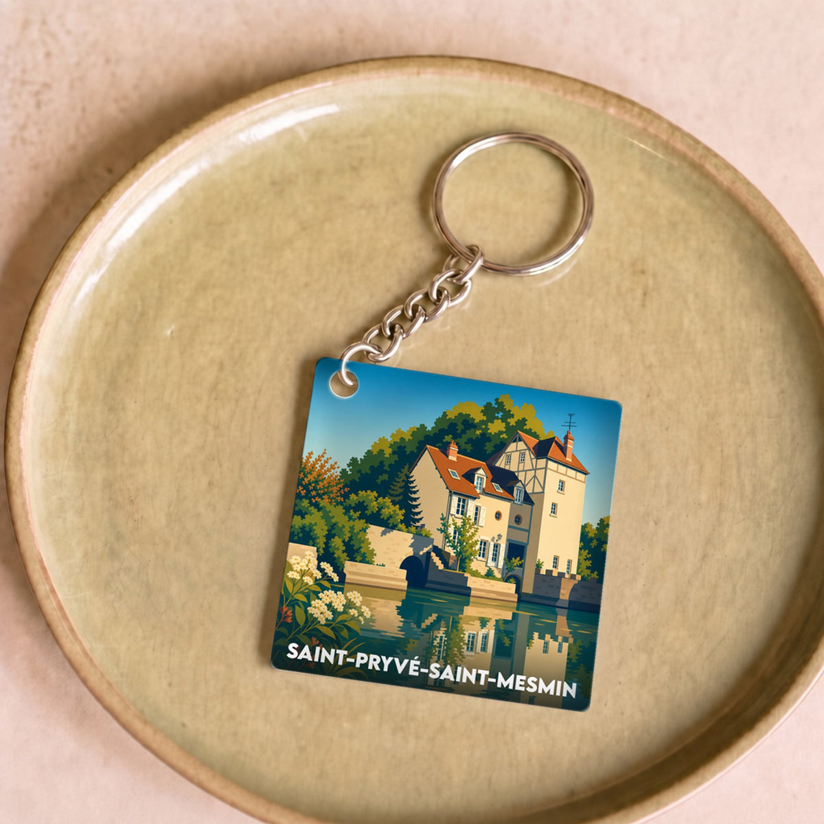 Porte-clés souvenir de la ville de Saint-Pryvé-Saint-Mesmin avec une illustration stylisée d'un manoir au bord de l'eau.