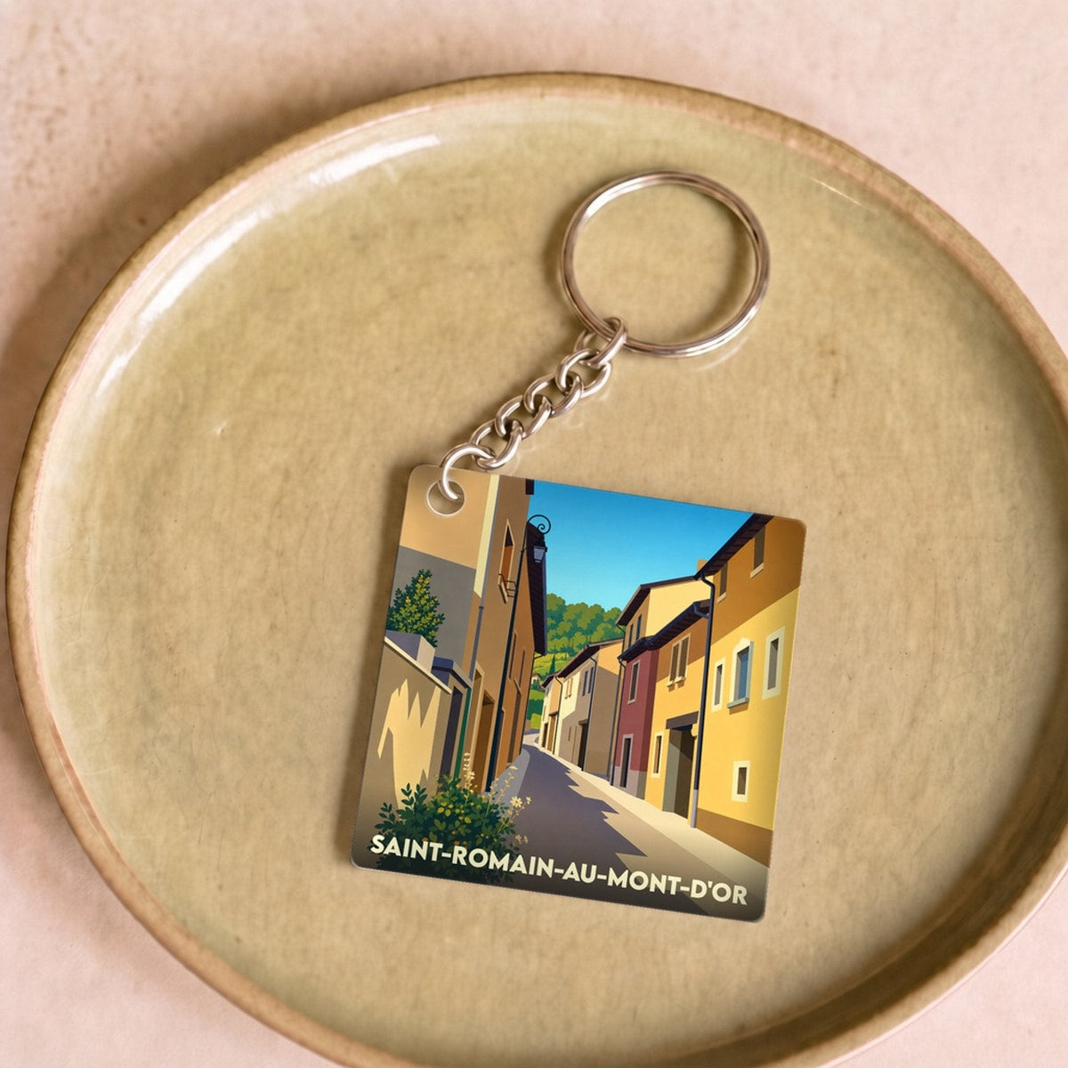 Porte-clés souvenir de la ville de Saint-Romain-au-Mont-d'Or avec une illustration stylisée d'une ruelle ensoleillée.