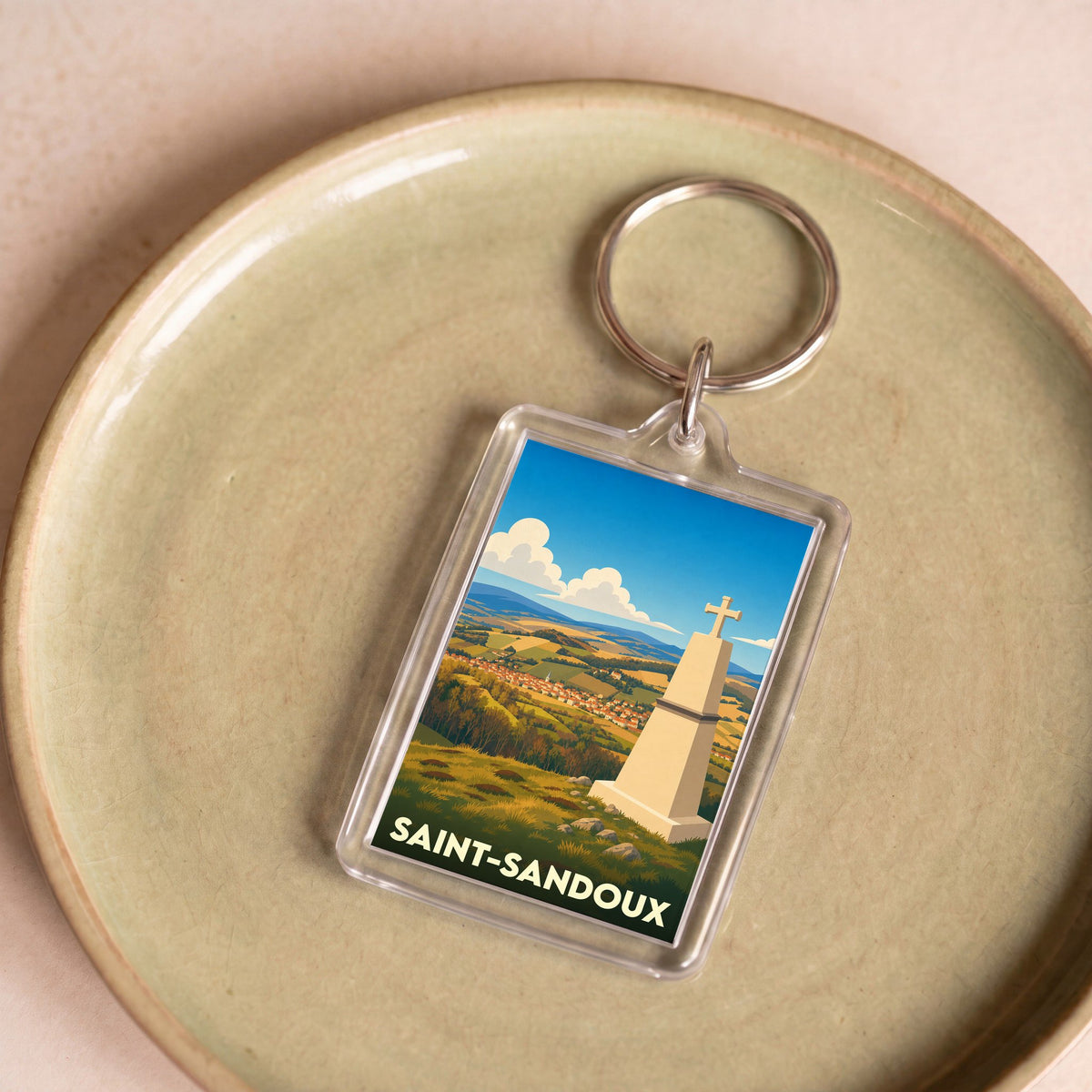 Porte-clés souvenir de la ville de Saint-Sandoux avec une illustration stylisée d'un monument et d'un paysage panoramique.