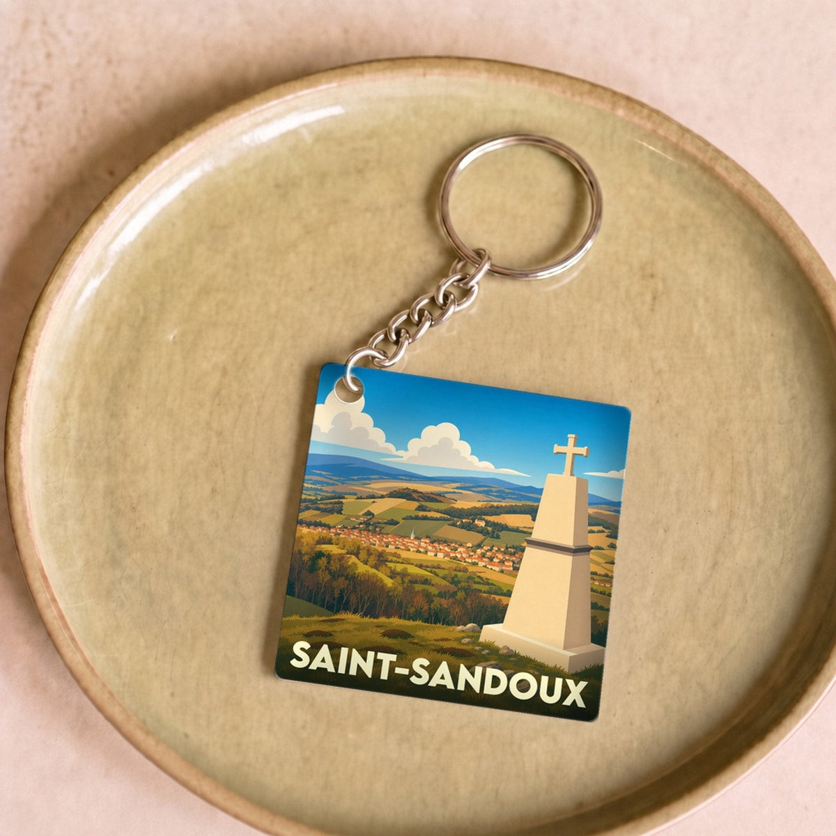 Porte-clés souvenir de la ville de Saint-Sandoux avec une illustration stylisée d'un monument et d'un paysage panoramique.