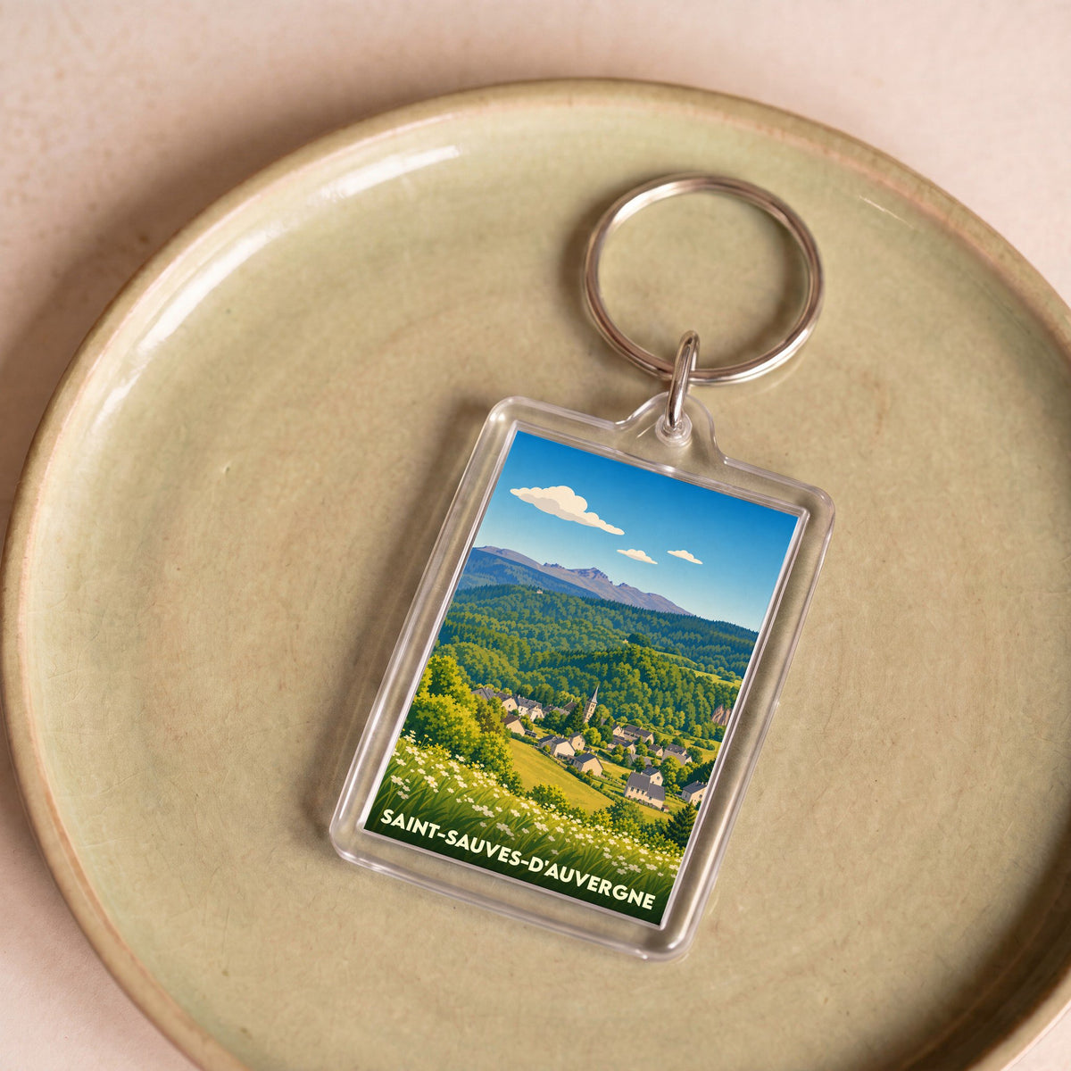 Porte-clés souvenir de Saint-Sauves-d'Auvergne avec une illustration stylisée du paysage local.