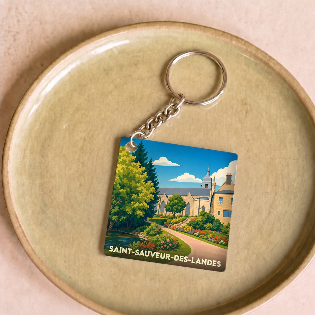 Porte-clés souvenir de la ville de Saint-Sauveur-des-Landes avec une illustration stylisée et colorée.