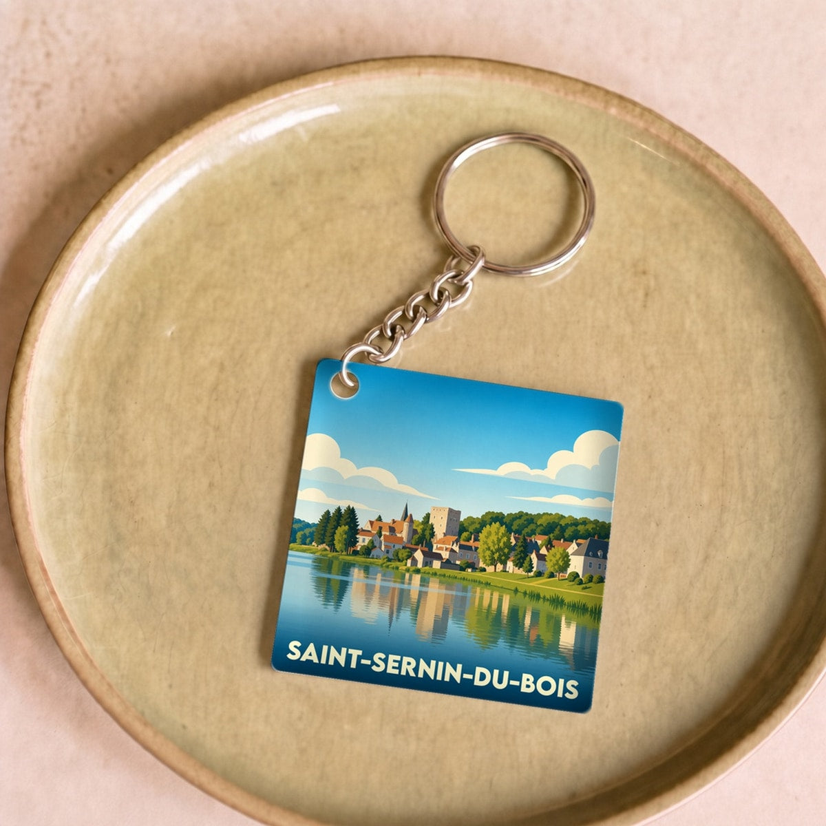 Porte-clés souvenir de la ville de Saint-Sernin-du-Bois avec une illustration stylisée d'un paysage au bord de l'eau.