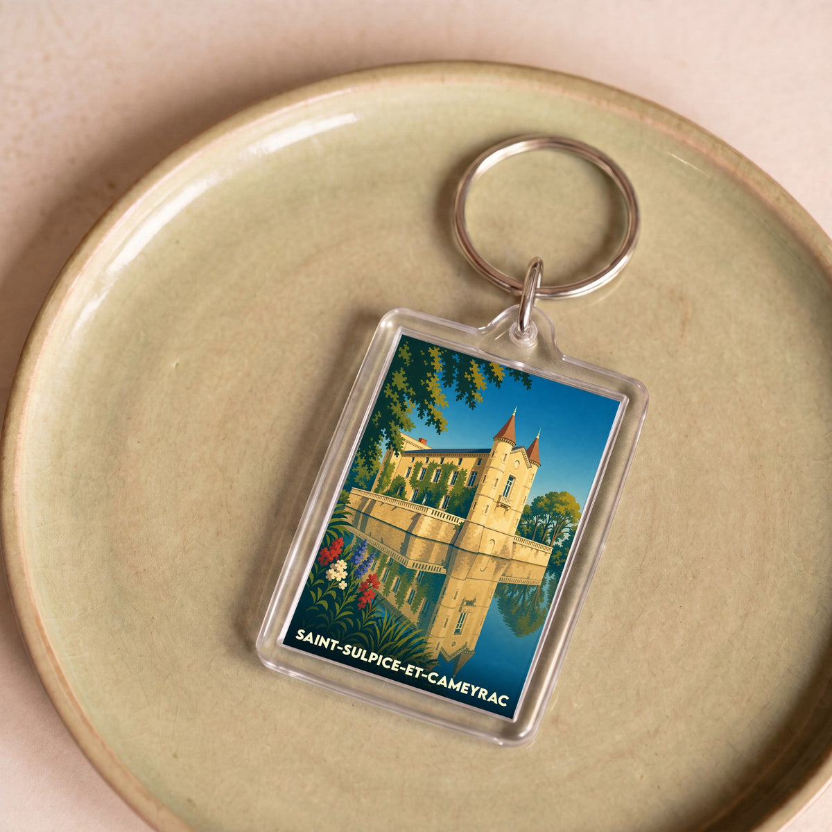 Porte-clés souvenir de Saint-Sulpice-et-Cameyrac avec une illustration stylisée d'un château se reflétant dans l'eau.