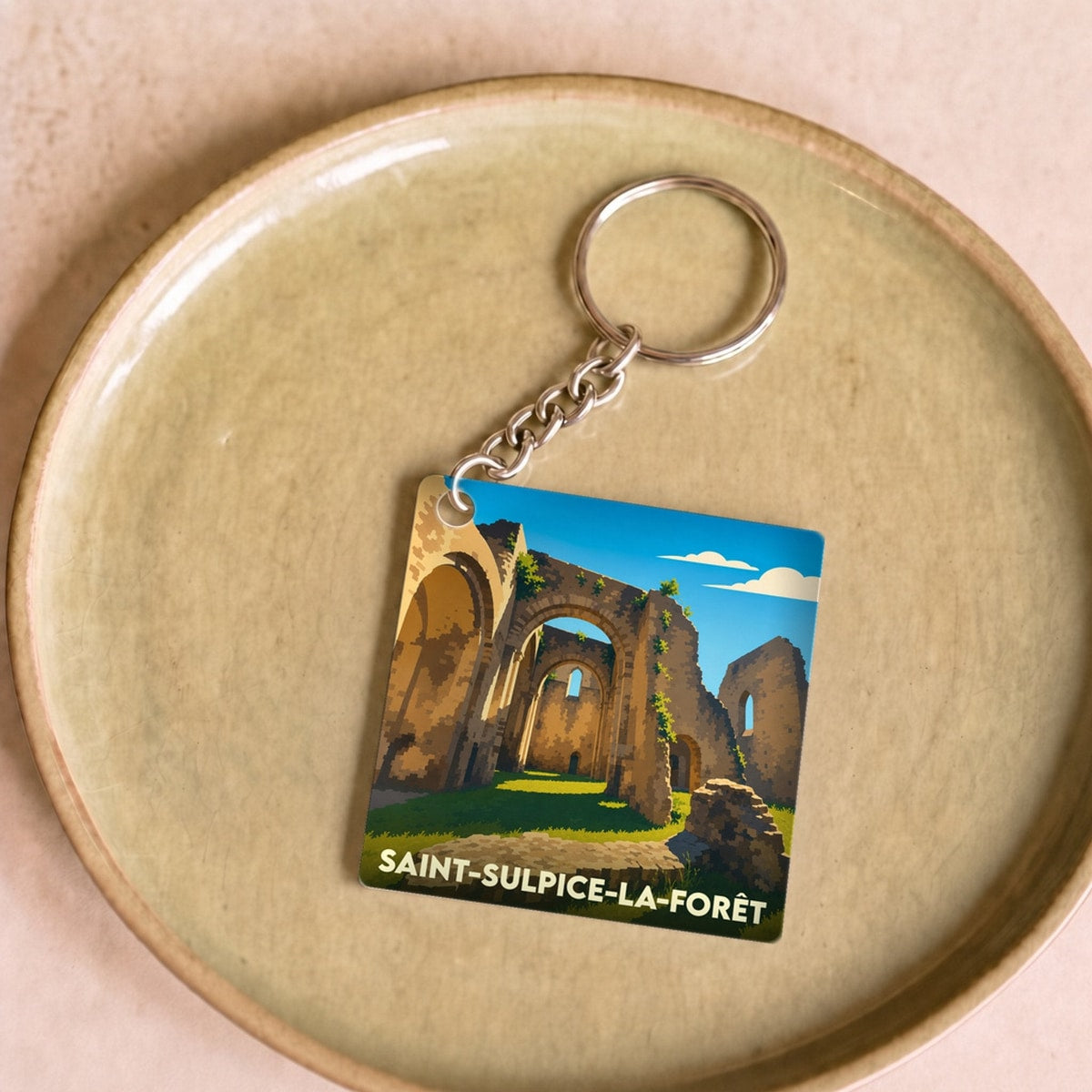 Porte-clés souvenir de la ville de Saint-Sulpice-la-Forêt avec une illustration stylisée d'une abbaye en ruines.