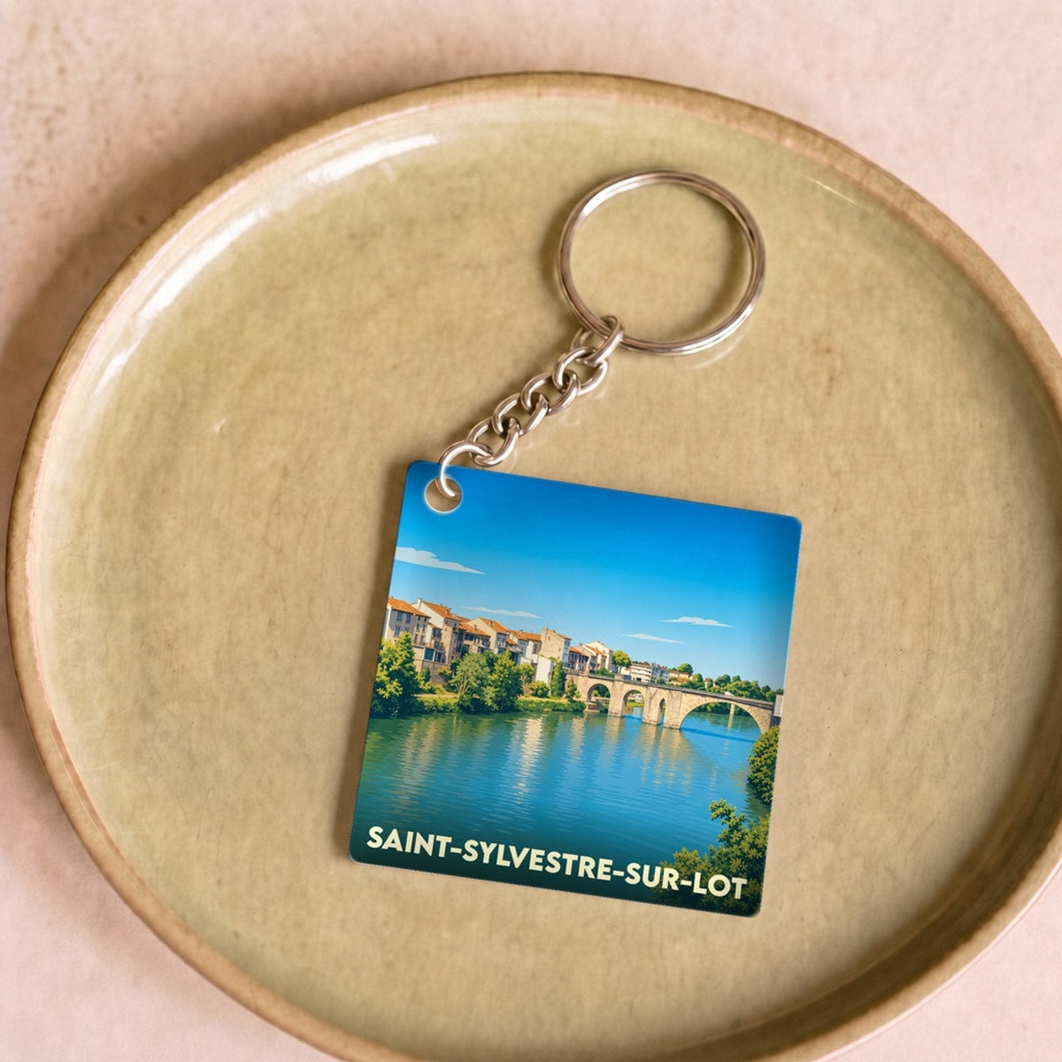 Porte-clés souvenir de la ville de Saint-Sylvestre-sur-Lot avec une illustration stylisée de son pont et de ses bords de rivière.
