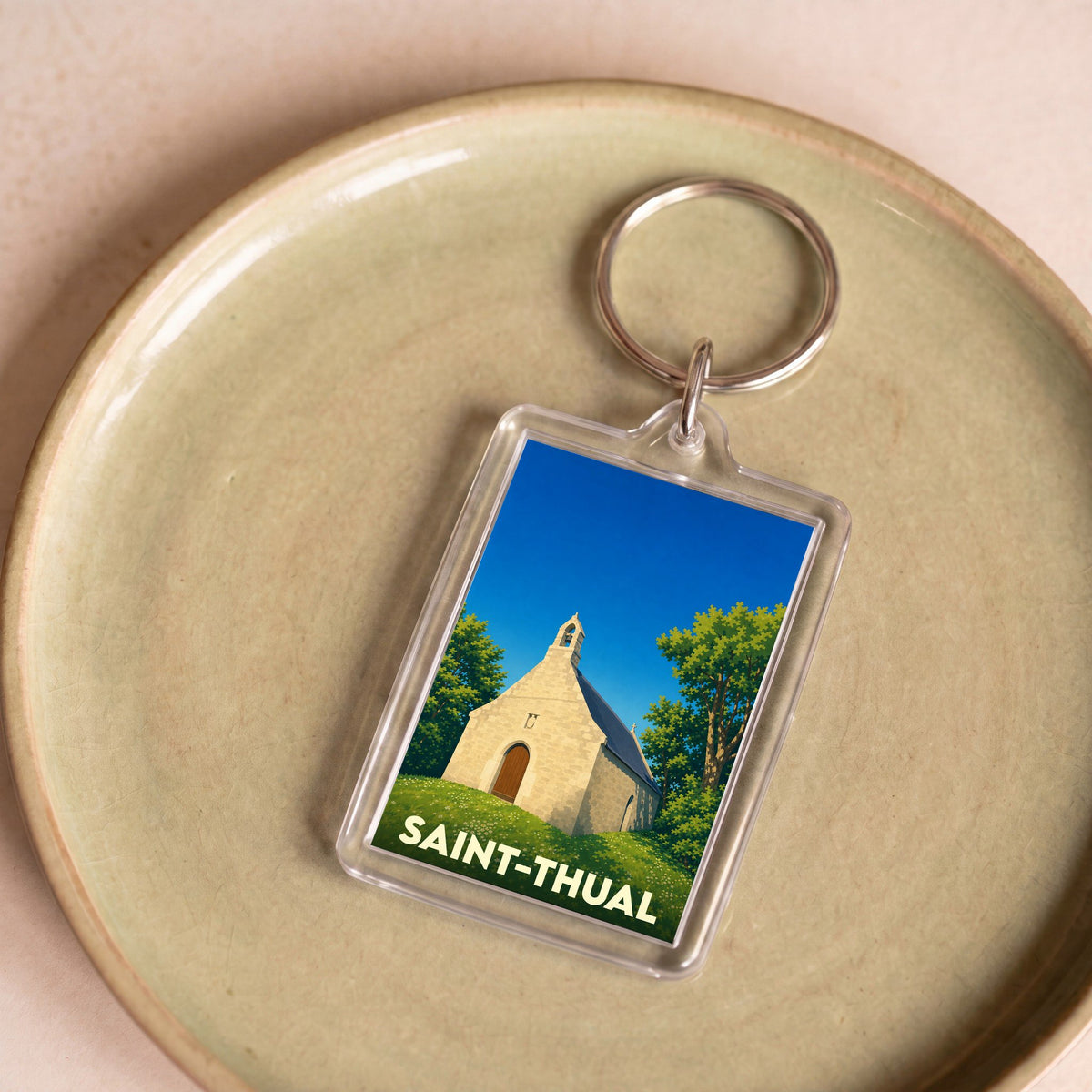 Porte-clés souvenir de la ville de Saint-Thual avec une illustration stylisée d'une petite chapelle.
