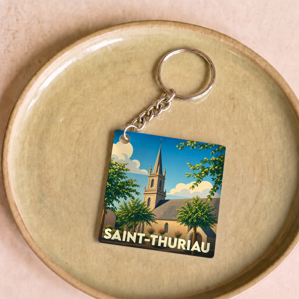 Porte-clés souvenir de la ville de Saint-Thuriau avec une illustration stylisée de son église sous un ciel bleu.