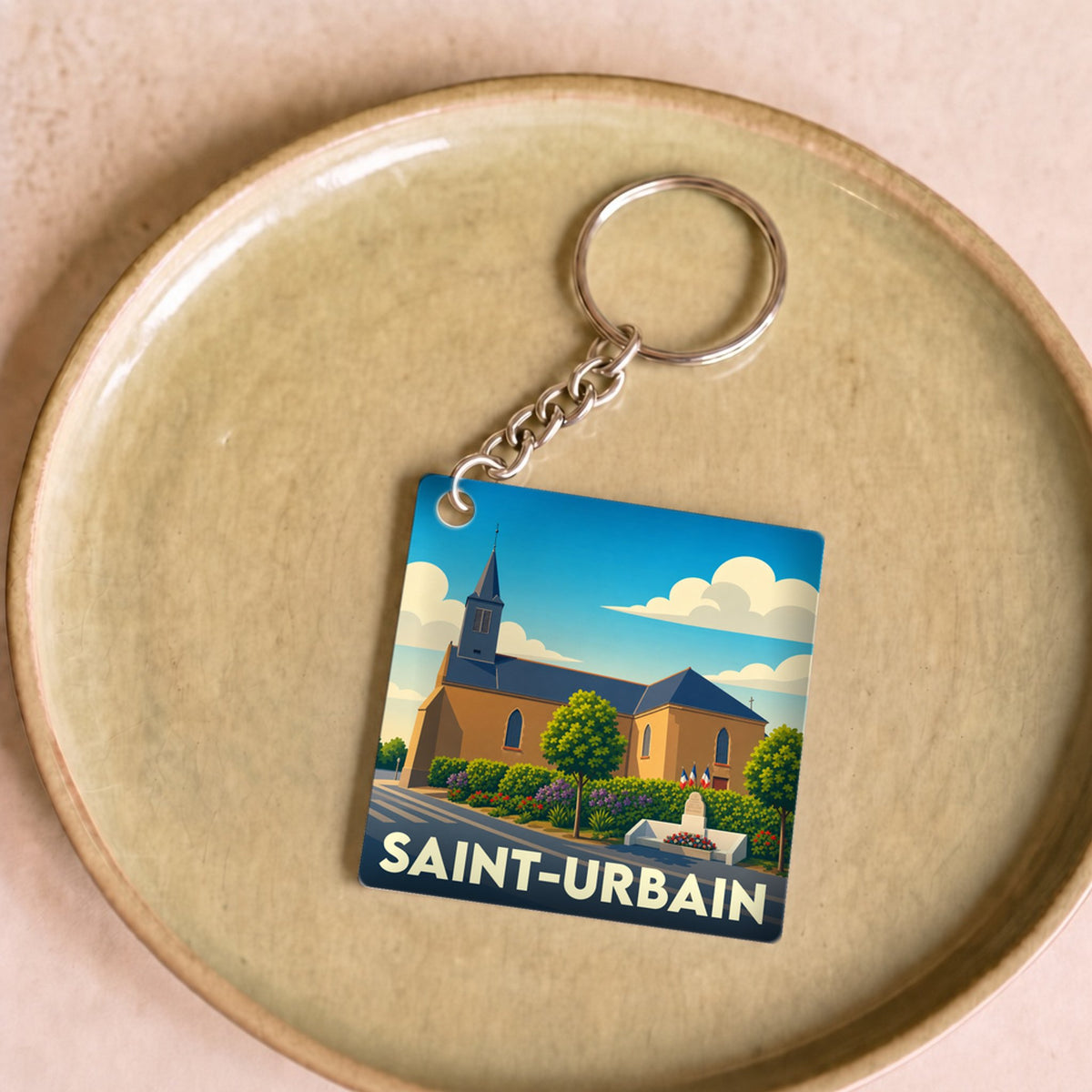 Porte-clés souvenir de la ville de Saint-Urbain avec une illustration stylisée de son église sous un ciel bleu.