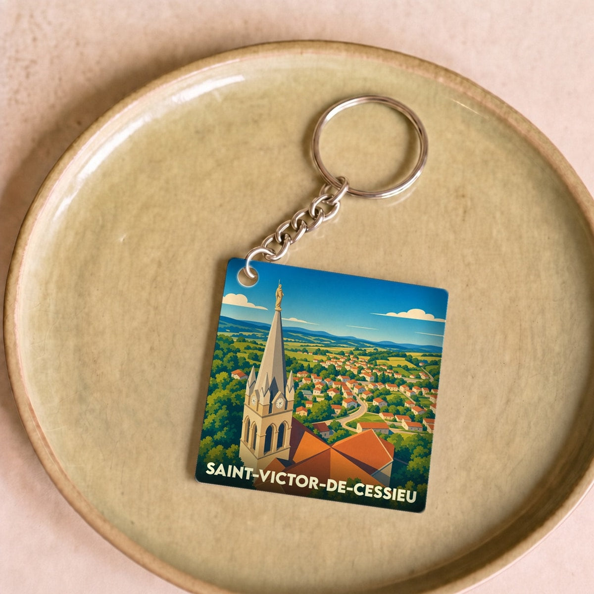 Porte-clés souvenir de la ville de Saint-Victor-de-Cessieu avec une illustration stylisée de son église et du paysage environnant.
