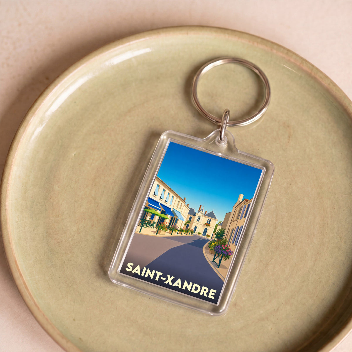 Porte-clés souvenir de la ville de Saint-Xandre avec une illustration stylisée d'une rue ensoleillée.