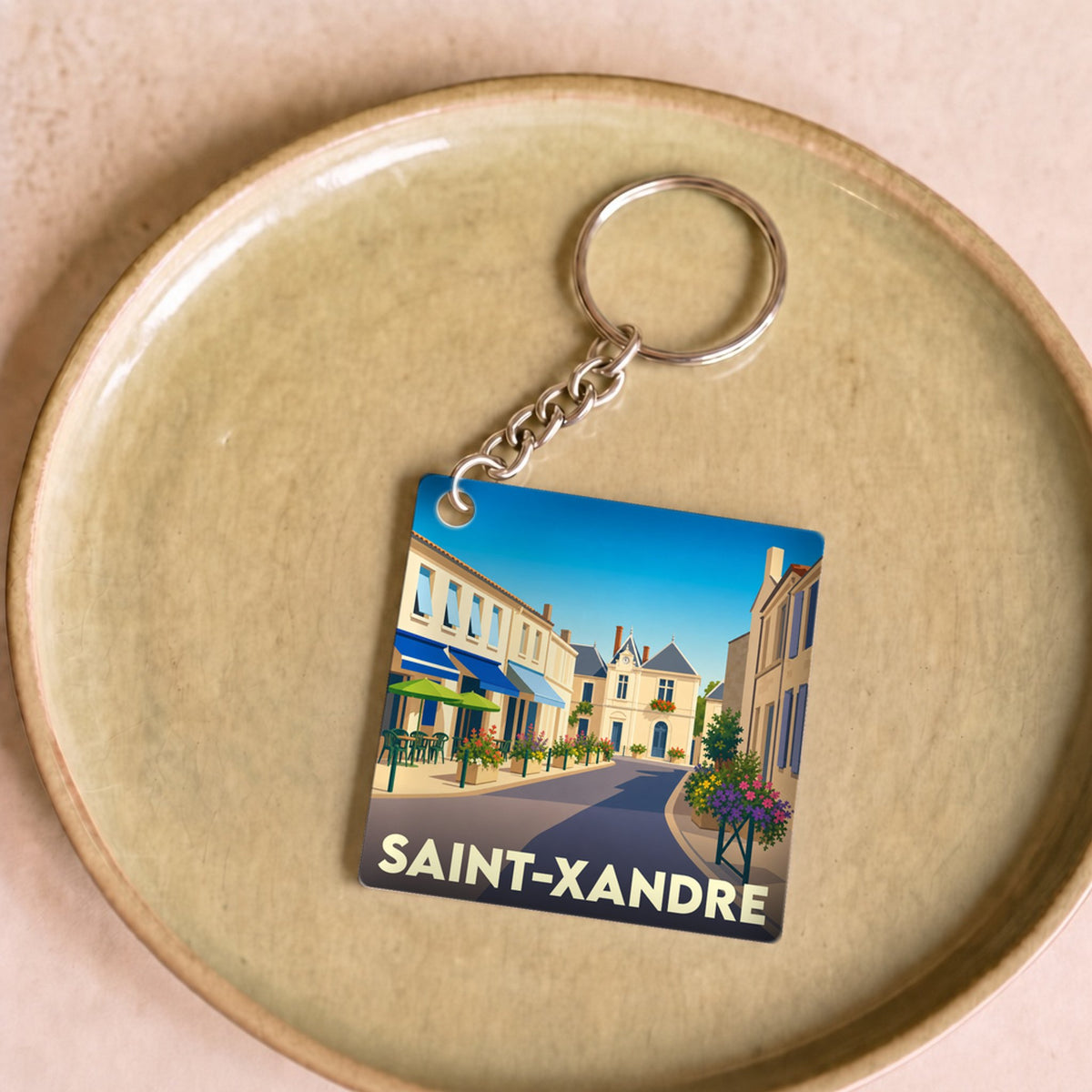 Porte-clés souvenir de la ville de Saint-Xandre avec une illustration stylisée d'une rue ensoleillée.