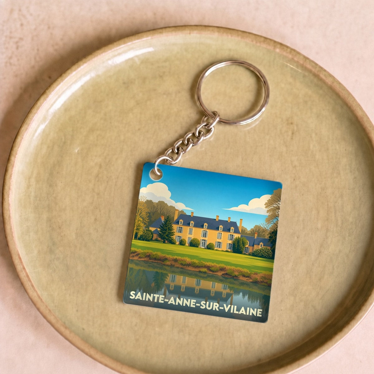Porte-clés souvenir de Sainte-Anne-sur-Vilaine avec une illustration stylisée d'un manoir se reflétant dans l'eau.
