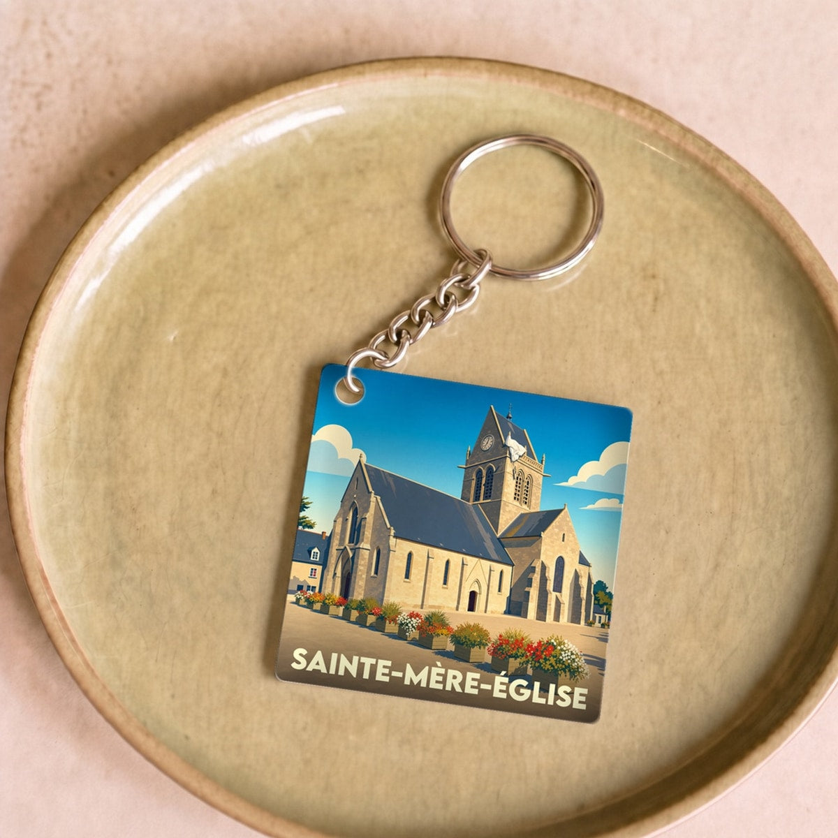 Porte-clés souvenir de la ville de Sainte-Mère-Église avec une illustration stylisée de son église.