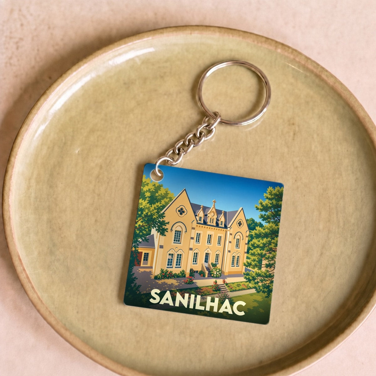 Porte-clés souvenir de la ville de Sanilhac avec une illustration stylisée d'une grande demeure.