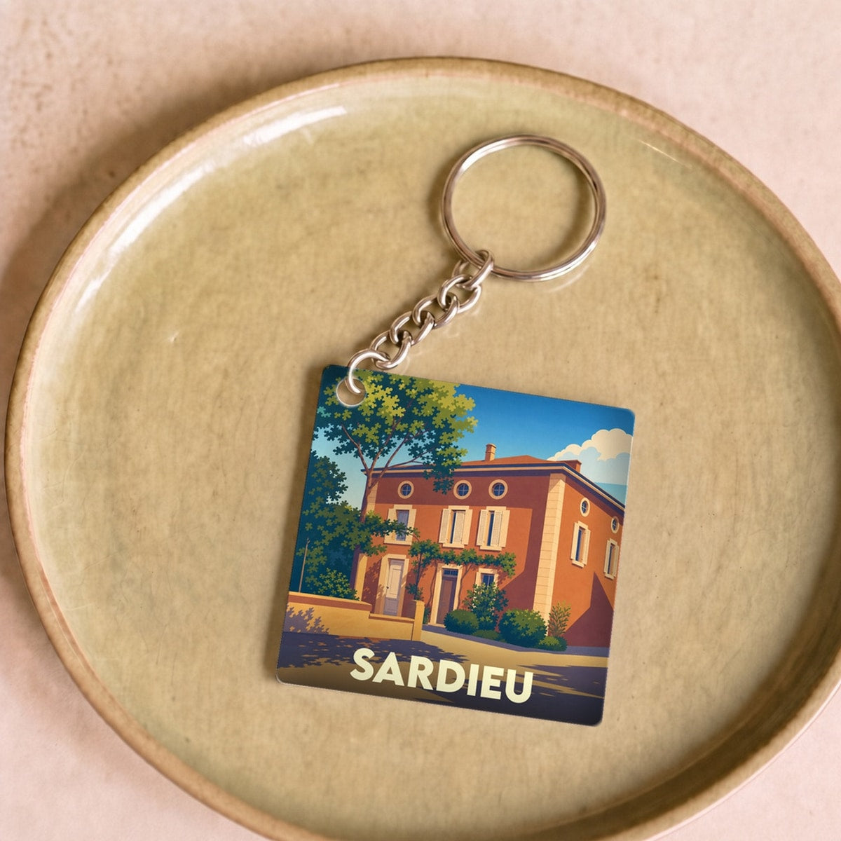Porte-clés souvenir de la ville de Sardieu avec une illustration stylisée d'une maison traditionnelle.