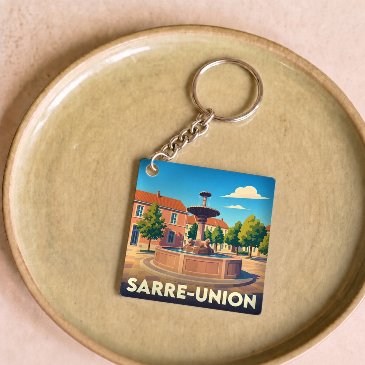 Porte-clés souvenir de la ville de Sarre-Union avec une illustration stylisée de sa place et sa fontaine.