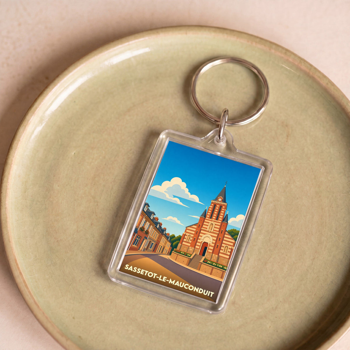 Porte-clés souvenir de Sassetot-le-Mauconduit avec une illustration stylisée de son église et de ses maisons.