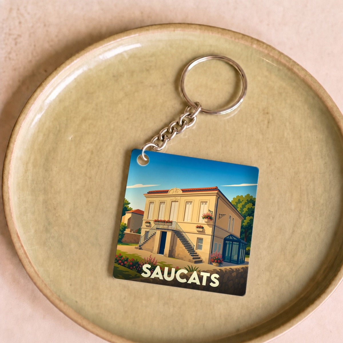 Porte-clés souvenir de la ville de Saucats avec une illustration stylisée d'une maison bourgeoise locale.