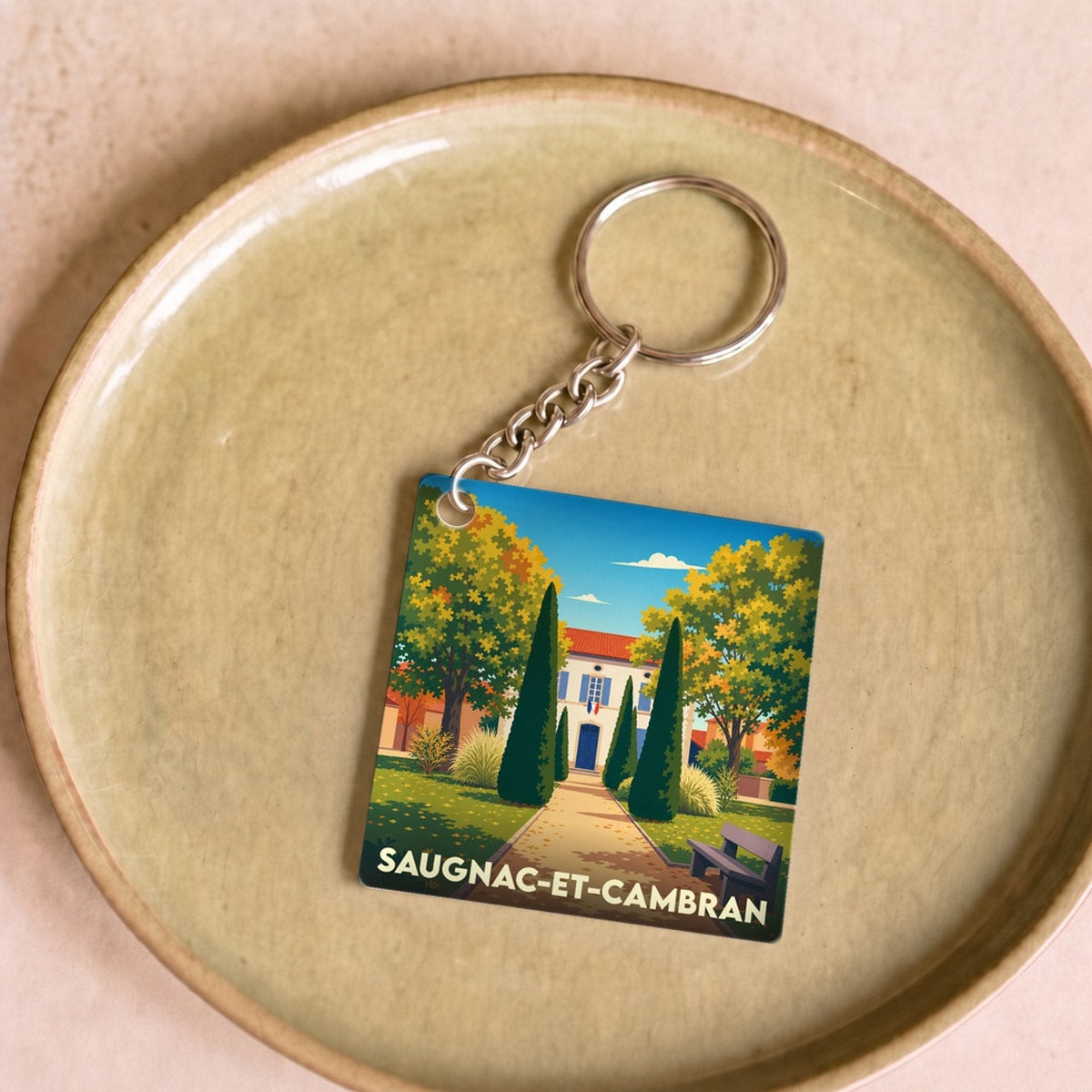 Porte-clés souvenir de la ville de Saugnac-et-Cambran avec une illustration stylisée d'un paysage ensoleillé.