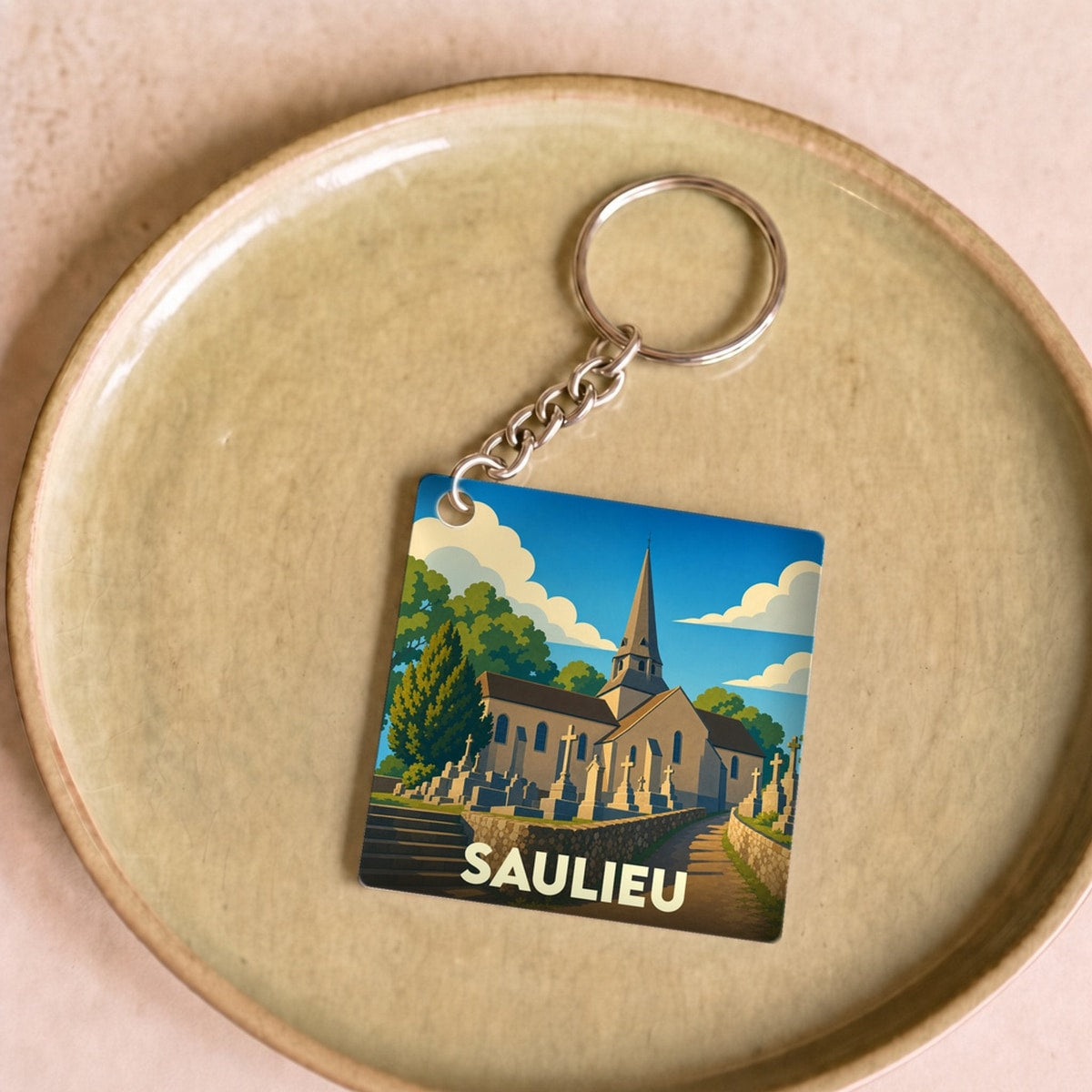 Porte-clés souvenir de la ville de Saulieu avec une illustration stylisée d'une église et de son cimetière.