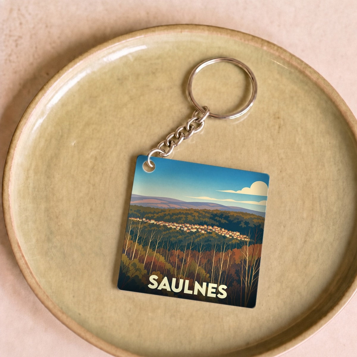 Porte-clés souvenir de la ville de Saulnes avec une illustration de paysage stylisée.