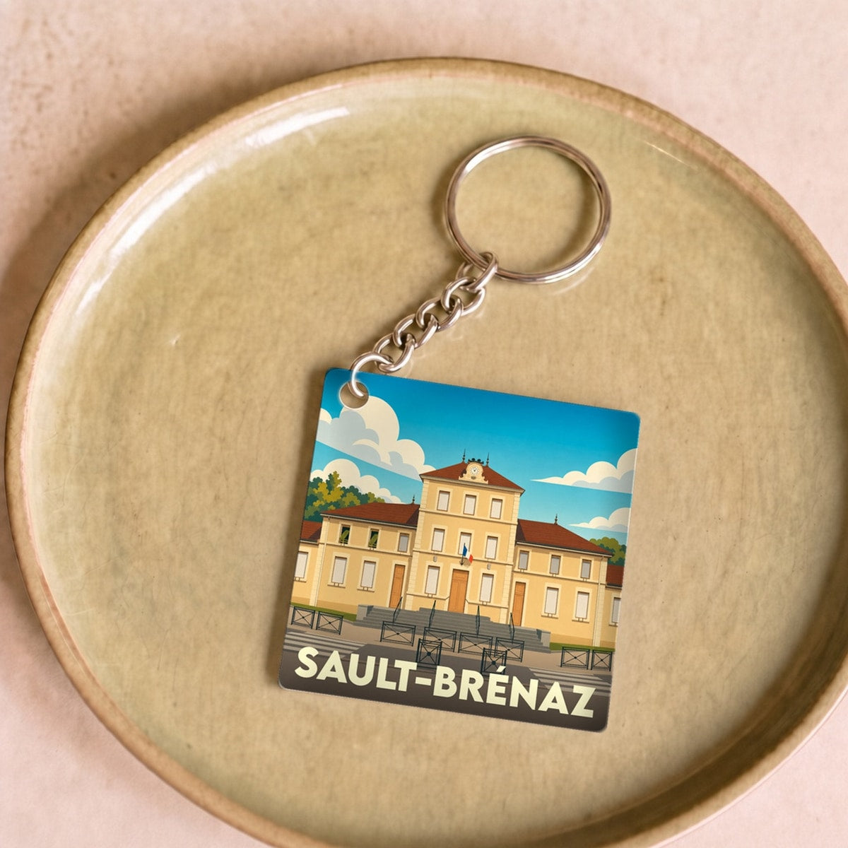 Porte-clés souvenir de la ville de Sault-Brénaz avec une illustration stylisée de sa mairie.